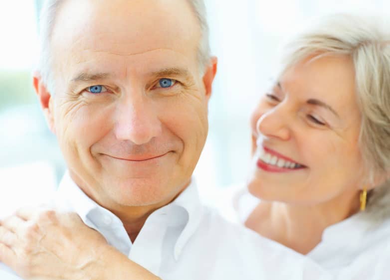 A happy old couple, the woman his behind the man holding him and smiling.