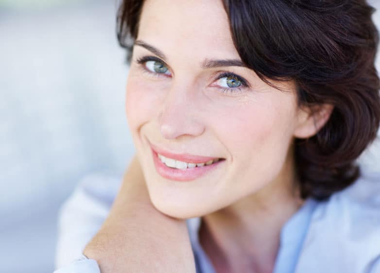 headshot of woman smiling with forearm under chin and blurred background