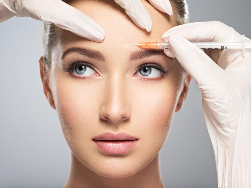 headshot of woman looking away as doctor in gloves puts cosmetic injection in her brow