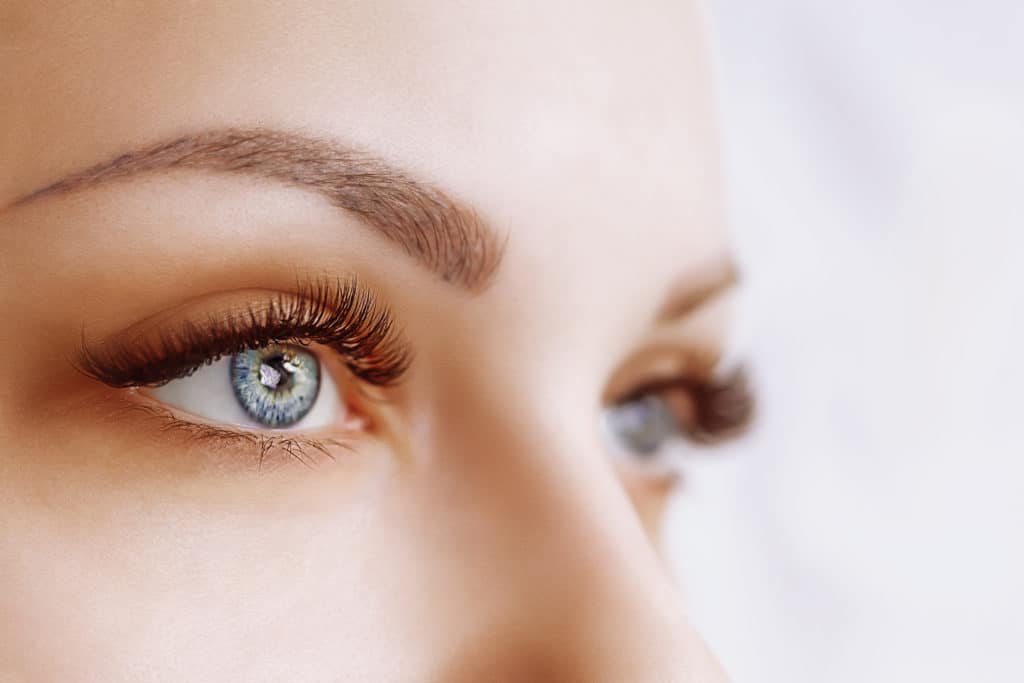 close up of woman's eyes shot at an angle from the side of her face showing large lashes and blurred background