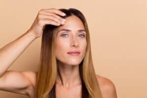 A middle age woman holds her hand to her forehead and looks concerned about skin sagging