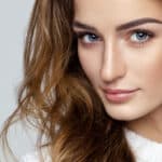 A close up of a woman's face with her wavy brown hair over her shoulder and she is making a serious but beautiful facial expresssion