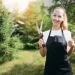 gardener girl in an apron and safety glasses holds garden scissors