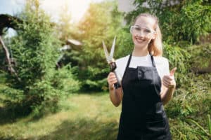 gardener girl in an apron and safety glasses holds garden scissors 