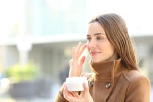 Satisfied woman applying moisturizer cream on her face in winter in the street