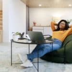 black woman in glasses relaxing on bean bag on break using laptop