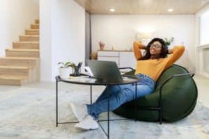 black woman in glasses relaxing on bean bag on break using laptop