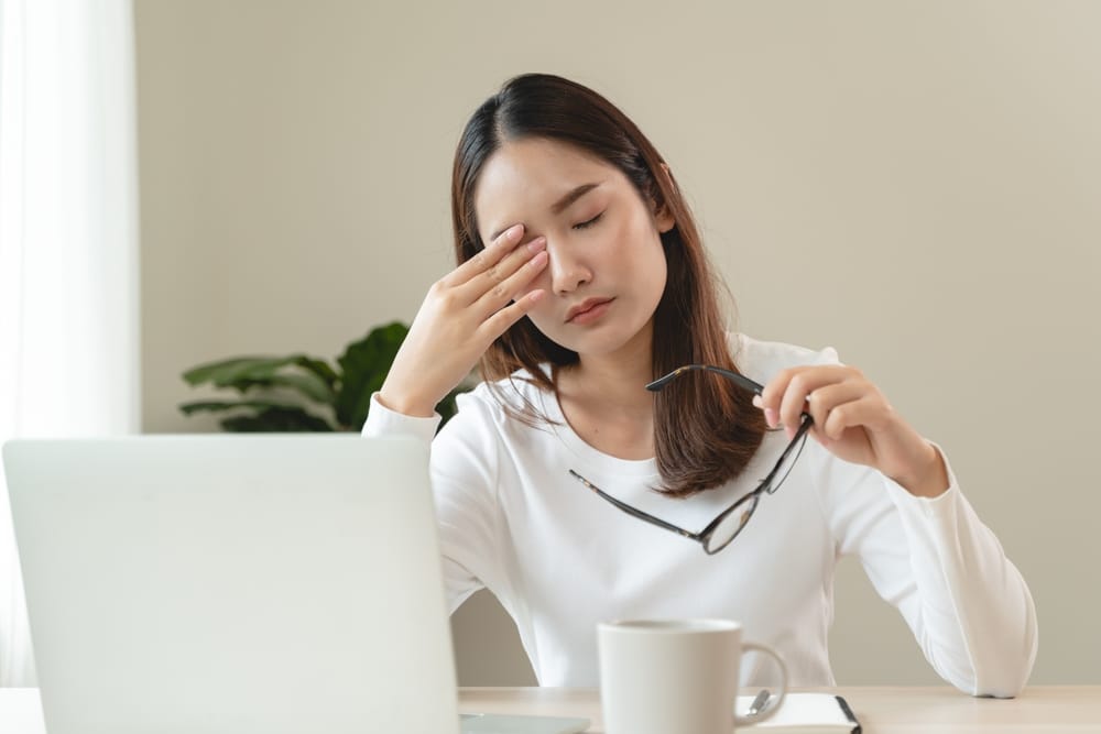 A woman with a migraine taking off her glasses and rubbing her eyes