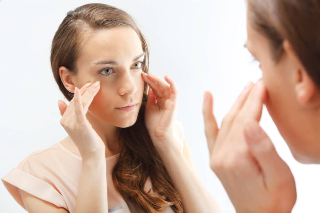 A woman with blepharospasm looking in the mirror considering surgery