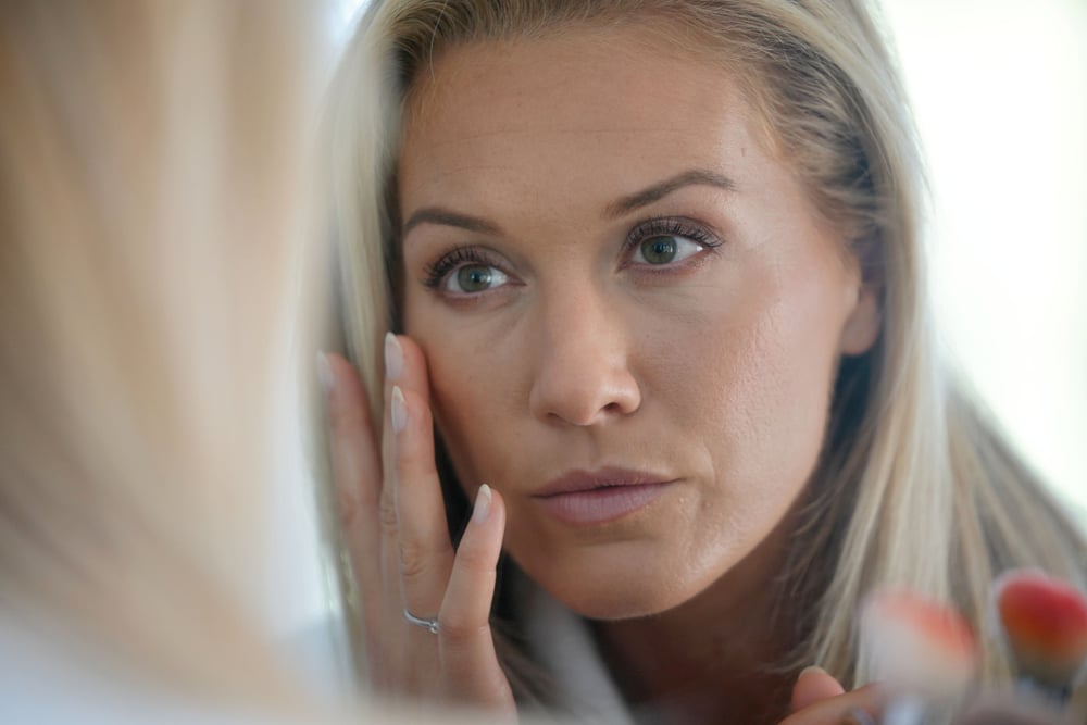 A woman looking in the mirror after eyelid cancer reconstruction surgery in St. Louis